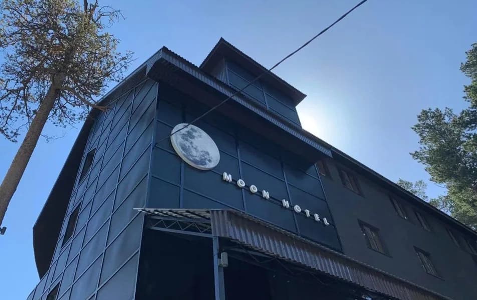 Дневной фасад Moon Hotel с балконами и соснами в Терсколе